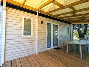 A covered deck with a table and chairs, wooden siding walls, and a sliding glass door. - Cozy mobile home - 6 guests (Saint-Hilaire-de-Riez)