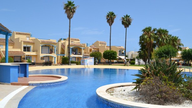 A swimming pool with a tiled edge, surrounded by palm trees and buildings with balconies. - Apartment with terrace - 4 guests (Vergel)