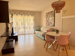 A modern living room with a dining area, a sofa, a table with chairs, a hanging light fixture, and a window with curtains. - Apartment with terrace - 4 guests (Vergel)