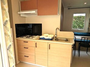 Een compacte keuken met een gasfornuis, een spoelbak en een raam met uitzicht op groen.
