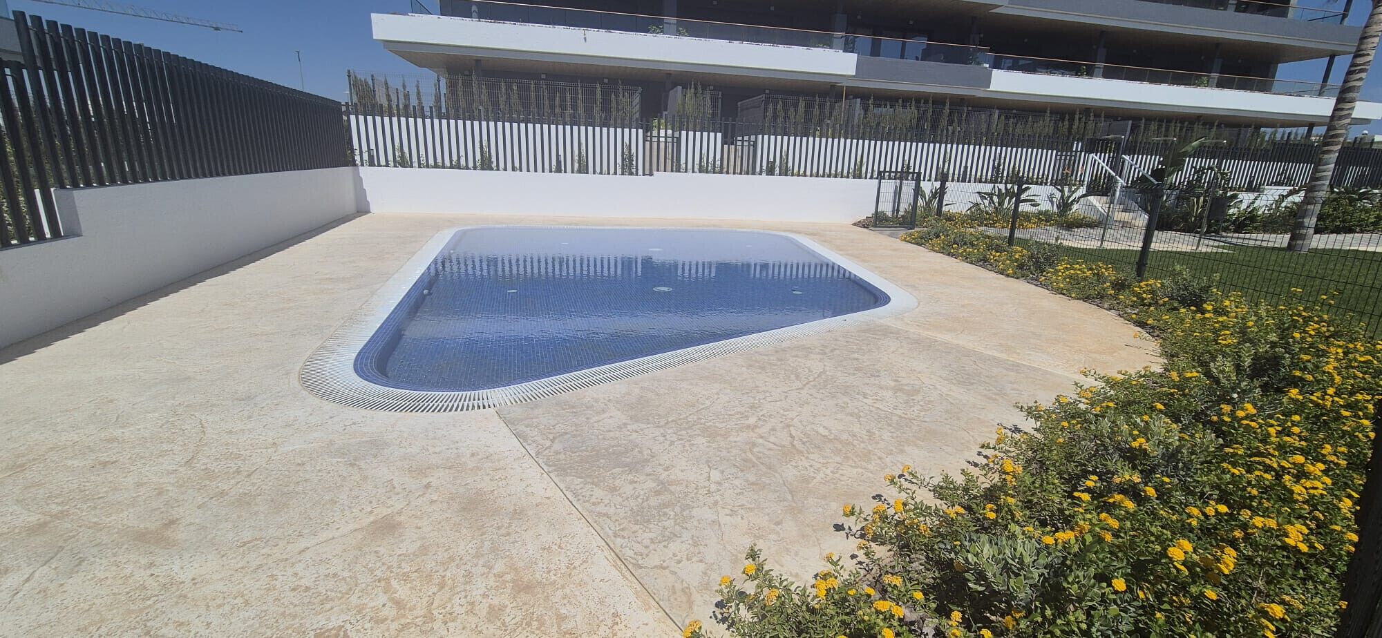 Una piscina de forma geométrica, rodeada por una terraza de concreto y una valla baja.