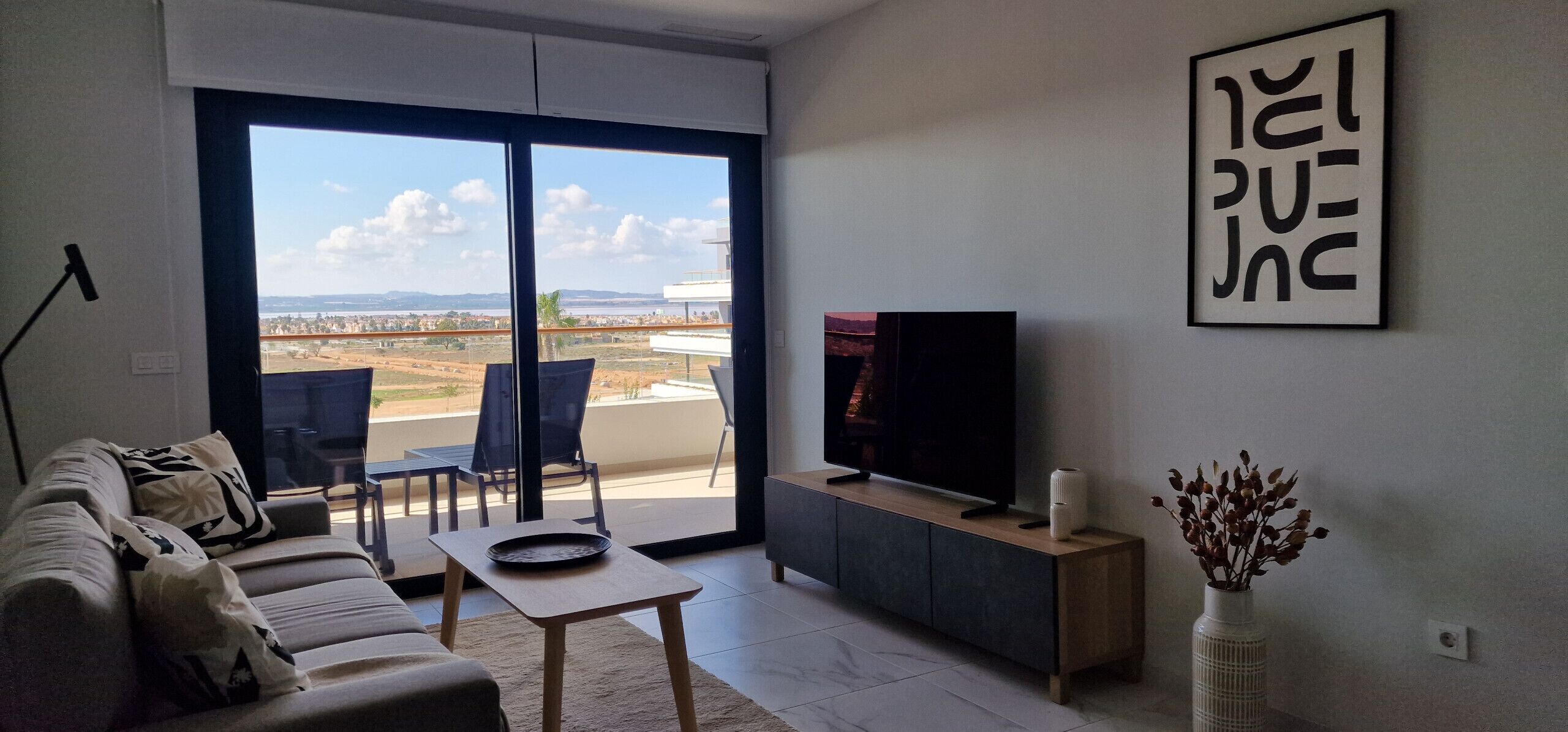 Una sala moderna con un sofá, una mesa de centro, un televisor sobre un mueble bajo y vistas a un espacio exterior a través de puertas correderas amplias.