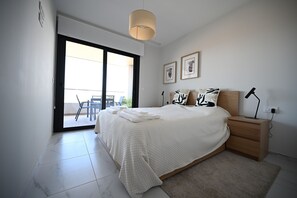 Ein Schlafzimmer mit einem Bett, einem Nachttisch, einer Lampe und Blick ins Freie.