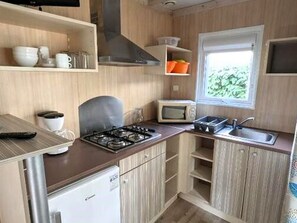 A compact kitchen with a gas stove, microwave, sink, and a small refrigerator. - Chalet, pets welcome - 4 guests (Saint-Hilaire-de-Riez)