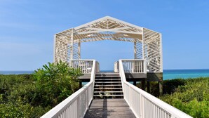 A wooden bridge leading to a white arched structure with a view of the ocean. - Luxury Seaside Home Steps to Private Beach Access, Renovated, Walk to Town (Santa Rosa Beach)