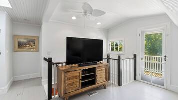 Une pièce avec un téléviseur posé sur un meuble en bois, un ventilateur de plafond et une porte donnant sur un balcon.