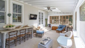 Eine überdachte Veranda mit Esstisch, Stühlen, einer Couch und einem Fernseher.