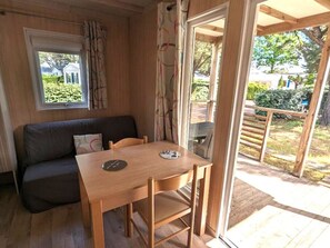 A cozy room with a wooden table, a sofa, and a sliding glass door leading to a patio. - Charming chalet, pets welcome - 2 guests (Saint-Hilaire-de-Riez)