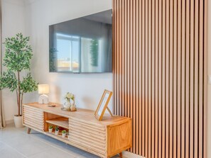 Ein modernes Wohnzimmer mit einem Holzkonsolentisch, einem flachbildfernseher an der Wand, einer Topfpflanze und einem Holzjalousi.