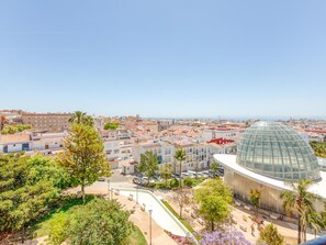 Ein modernes Gebäude mit einer Glaskuppel, umgeben von einem angelegten Garten und Blick auf eine Küstenstadt.