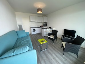 A compact living space with a sofa, a small coffee table, a TV, and a kitchenette area. - Studio sea view - 2 guests (Arcachon)