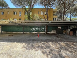 Ein Gebäude mit grüner Fassade, einem überdachten Parkplatz und Bäumen im Hintergrund.