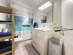 Ein Badezimmer mit einer maritime gestalteten Duschvorhangs, einem Waschbecken mit Spiegel, einem Handtuchhalter und einem Wäschekorb.