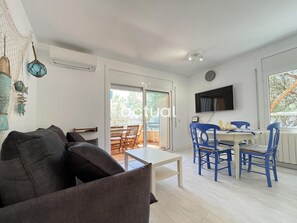 A modern living room with a sofa, a dining area with blue chairs, a TV mounted on the wall, and a balcony with a view. - Charming apartment with AC, parking - 4 guests (Platja d'Aro)