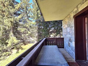 Ein Balkon mit Steinwand, Holzgeländer und Blick auf Bäume.
