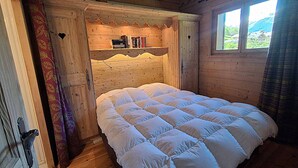 Ein Schlafzimmer einer Holzhütte mit einem Bett, einem Bücherregal und einem Fenster.