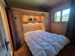 Ein Schlafzimmer einer Holzhütte mit einem Bett, einem Bücherregal und einem Fenster.