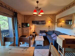 Interior de una cabaña de madera con sofá, mesa, sillas, televisor y chimenea.