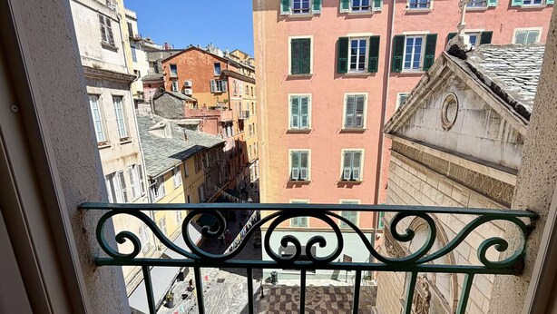 Un balcón con barandilla de hierro forjado que da a una calle urbana con edificios históricos.