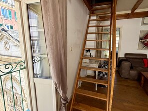 Une échelle en bois dans une pièce avec une fenêtre, un canapé et une petite table.