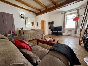 Un salon avec un canapé, une table basse, un téléviseur et une fenêtre avec des rideaux.