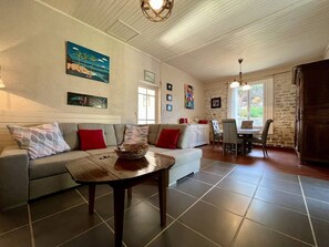 A living room with a sofa, a coffee table, and a dining area with chairs and a table. - Spacious house in quiet area - 6 guests (Saint-Georges-d'Oléron)
