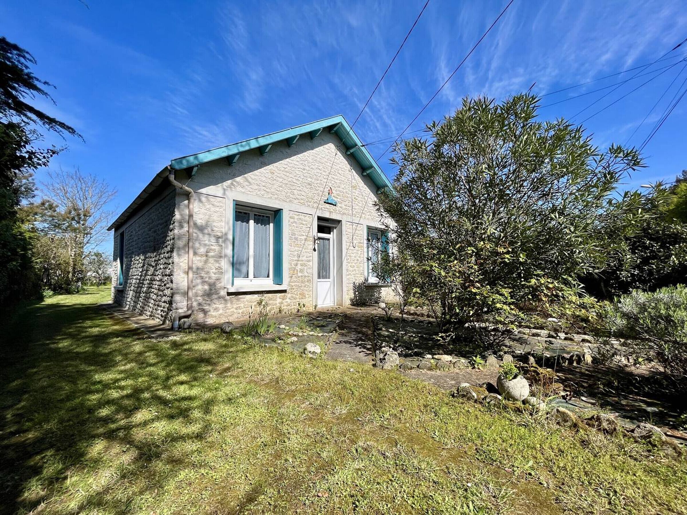 A stone house with a blue roof, a small porch, and a garden with rocks and plants.