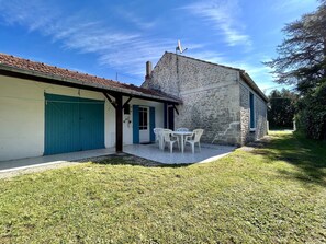 A stone building with a tiled roof, a blue garage door, and a patio with white chairs. - Spacious house in quiet area - 6 guests (Saint-Georges-d'Oléron)