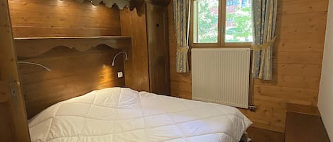 A wooden room with a bed, a window with curtains, and a radiator.