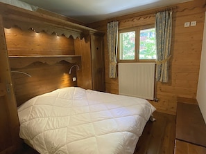 Ein Zimmer mit Holzboden, einem Bett, einem Fenster mit Vorhängen und einer Heizung.