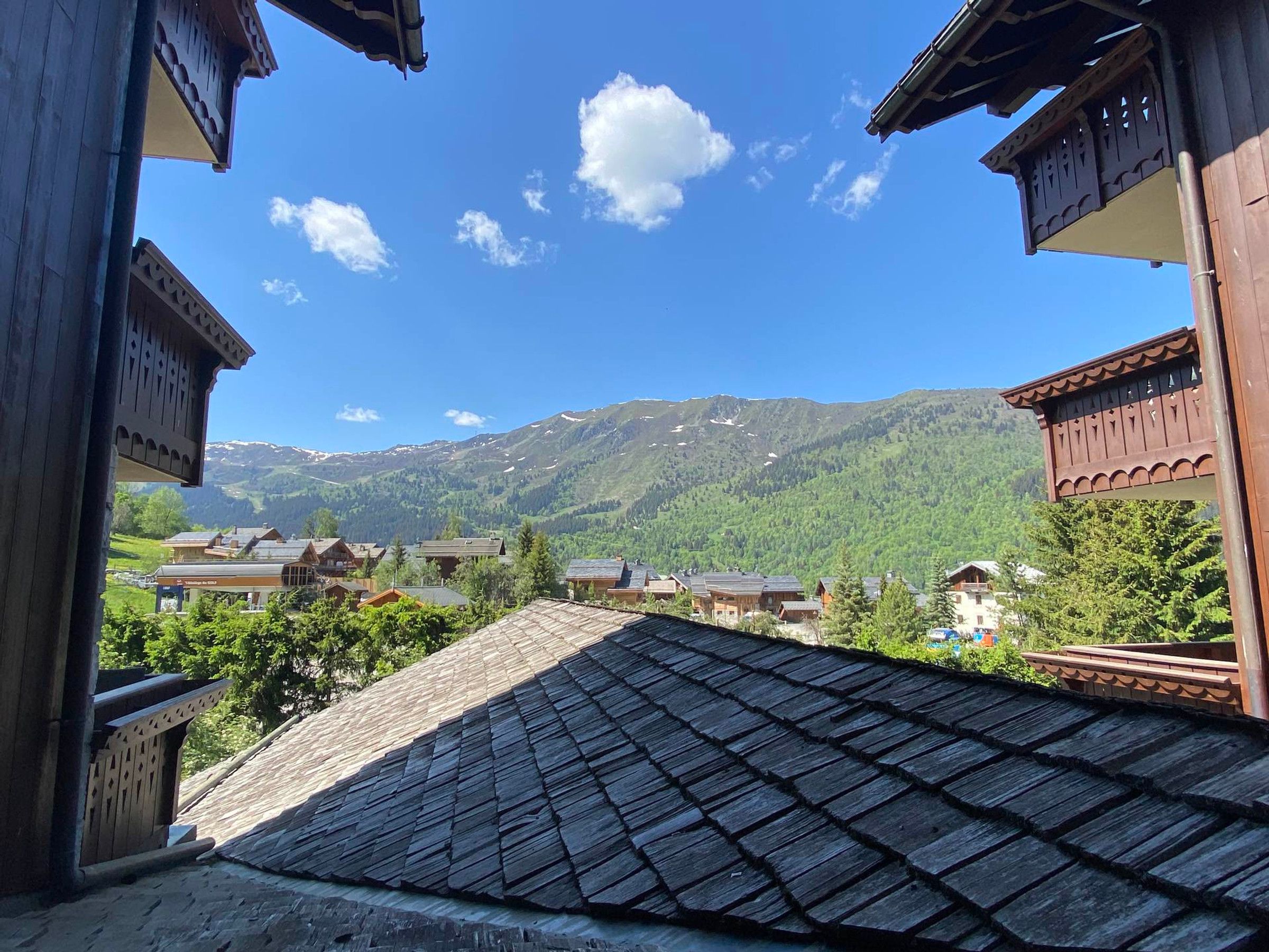 A view of a mountain village with traditional wooden buildings, a clear sky, and snow-capped mountains in the background.