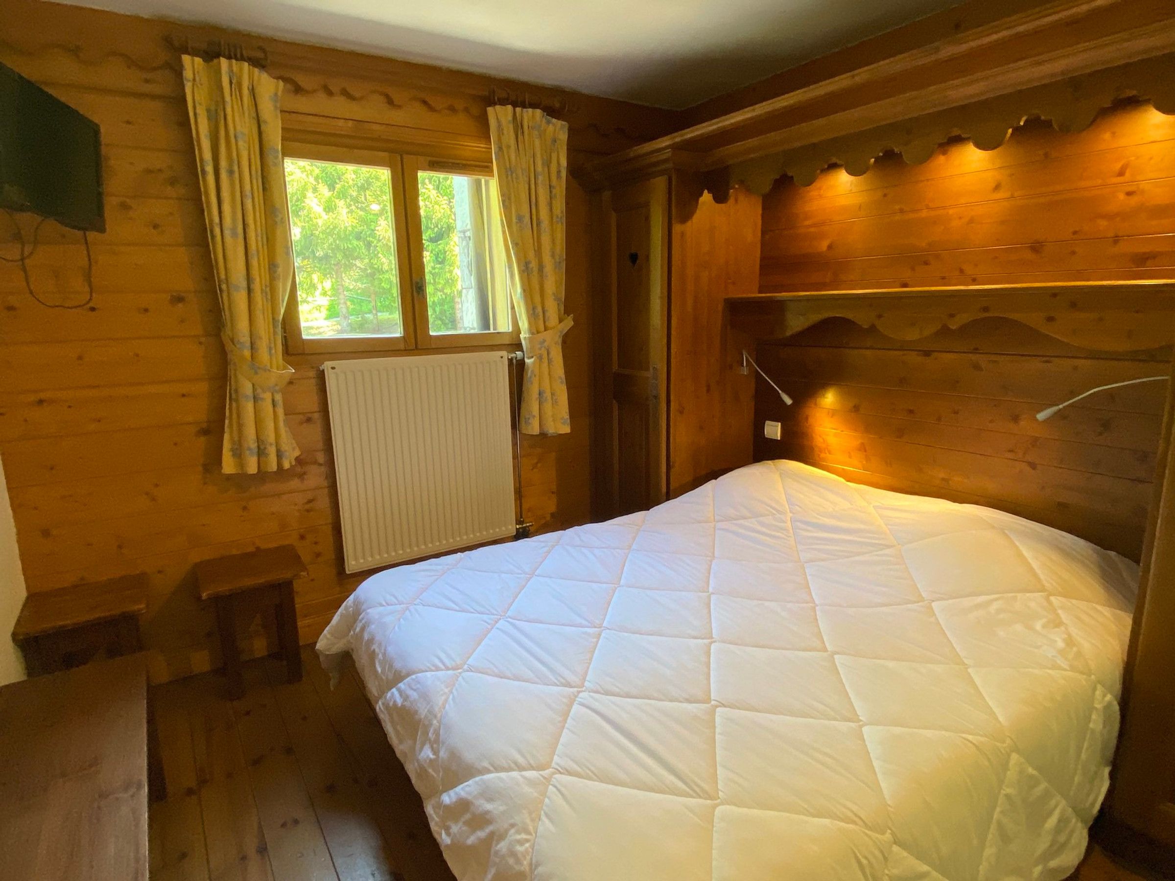Una camera in una baita di legno con un letto, una finestra con tende, un termosifone e una testiera in legno.
