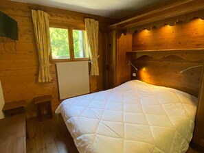 Une pièce de type cabane en bois, avec un lit, une fenêtre avec des rideaux, un radiateur et une tête de lit en bois.