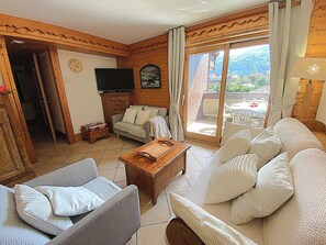 Un salon confortable avec un canapé, un fauteuil, une table basse en bois et un téléviseur.