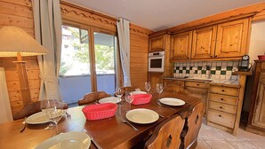 Een houten eettafel gedekt met borden, glazen en bestek, een rode mand en een raam met gordijnen.