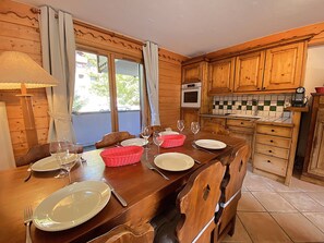 Ein Esszimmer mit einem Holztisch, gedeckten Tellern, Gläsern und Besteck, einem roten Korb und einem Fenster mit Vorhängen.