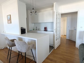 Eine moderne Küche mit weißen Schränken, einer Bar mit zwei Barhocker und einer Kaffeemaschine.