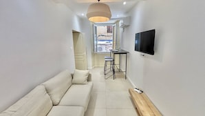 A modern living room with a sofa, a TV mounted on the wall, and a window with a view. - Apartment with air conditioning, central Ajaccio (Ajaccio)
