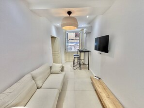 A modern living room with a sofa, a TV mounted on the wall, and a window with a view. - Apartment with air conditioning, central Ajaccio (Ajaccio)