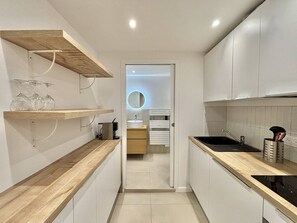 A modern kitchen with wooden countertops, a black sink, and a built-in oven. There are shelves with glassware and a coffee machine. - Apartment with air conditioning, central Ajaccio (Ajaccio)