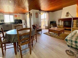 A cozy living room with a wooden ceiling, a dining area with a table and chairs, a sofa, a fireplace, and a TV. - Unique house, pond view - 4 guests (Mèze)
