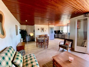 A cozy living room with a wooden ceiling, a dining area with a table and chairs, and a kitchen in the background. - Unique house, pond view - 4 guests (Mèze)
