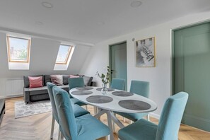 Un espace repas moderne avec une table ronde, des chaises de couleur turquoise et un canapé gris en arrière-plan.