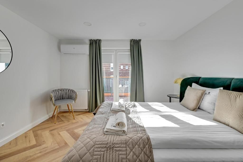 A bedroom with a bed, a chair, a window with curtains, and an air conditioning unit.