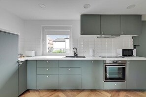 Une cuisine moderne avec des meubles gris, un plan de travail blanc, un four encastré et une fenêtre qui laisse entrer la lumière naturelle.