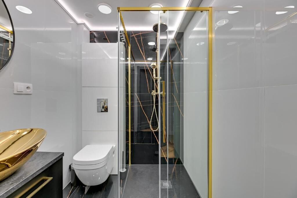A modern bathroom with a glass-enclosed shower, a toilet, and a vanity with a gold bowl.