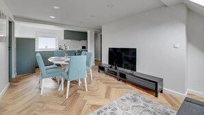 Una sala de estar moderna con comedor, televisor de pantalla plana y cocina al fondo.