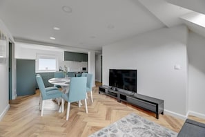 Un salon moderne avec un coin repas, un téléviseur à écran plat et une cuisine en arrière-plan.