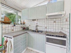 Eine kleine Küche mit Einbauofen, Spüle und Fenster mit Blick auf Grünflächen.
