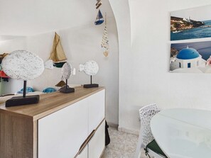Ein Zimmer mit Holztresen, weißen Schränken, einem weißen Stuhl, einem kleinen Tisch und einem Wandbild mit einer Küstenansicht.